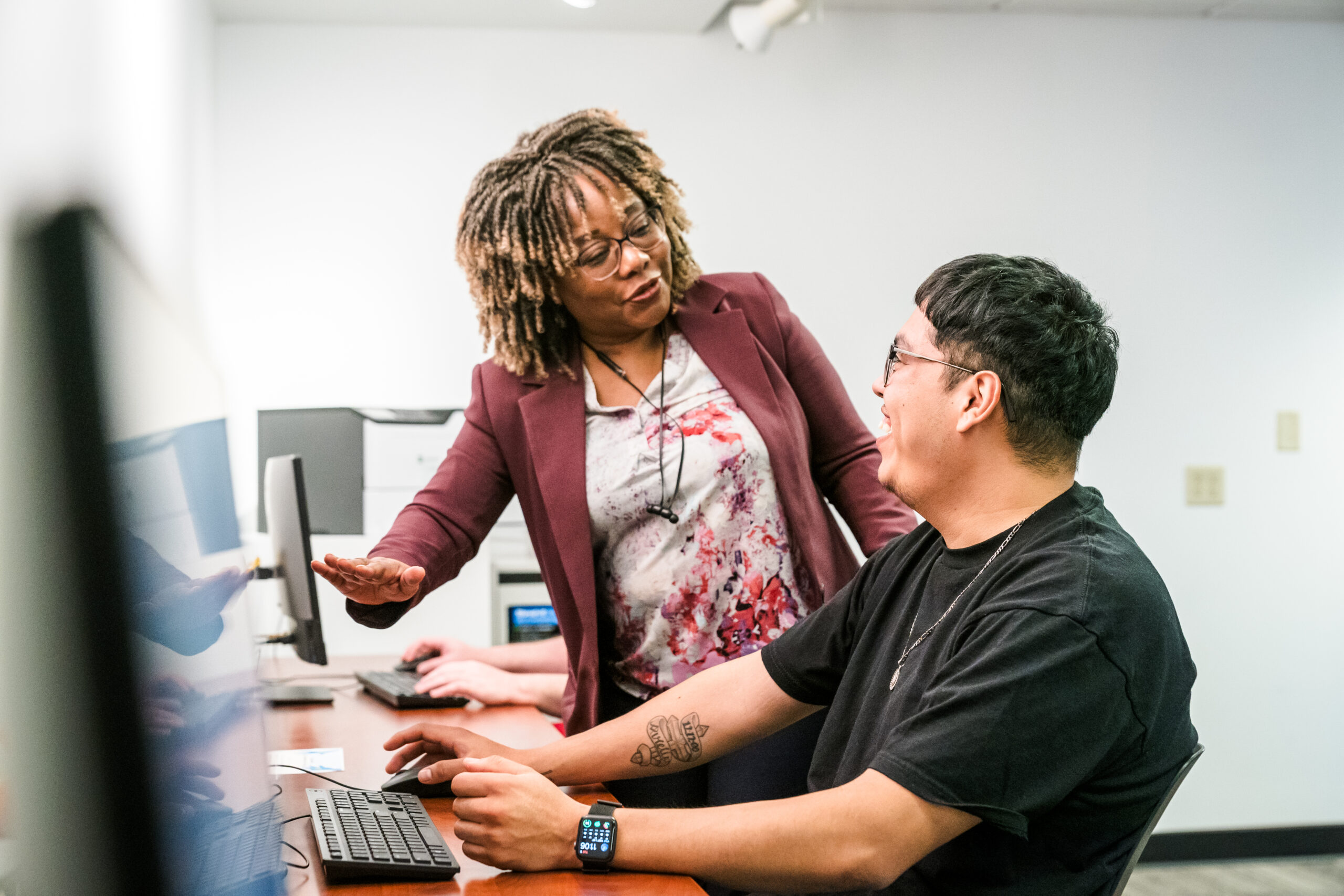 An instructor standing next to a student working on a computer.