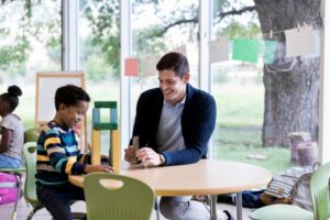 A special education teacher sitting at a table with a student while building with blocks.