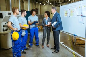 An operations manager talking to a team of workers in a manufacturing facility.