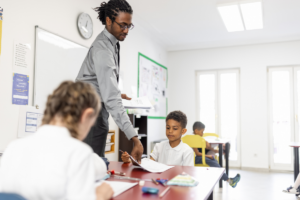 An elementary school teacher hands out assignments in a classroom.