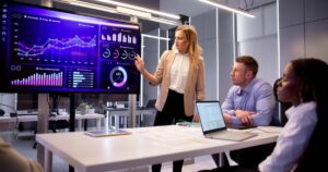 A business intelligence analyst gives a presentation using a data visualization dashboard displayed on a monitor.